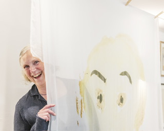 The artist peeks out from behind a silk screen print of a woman’s face